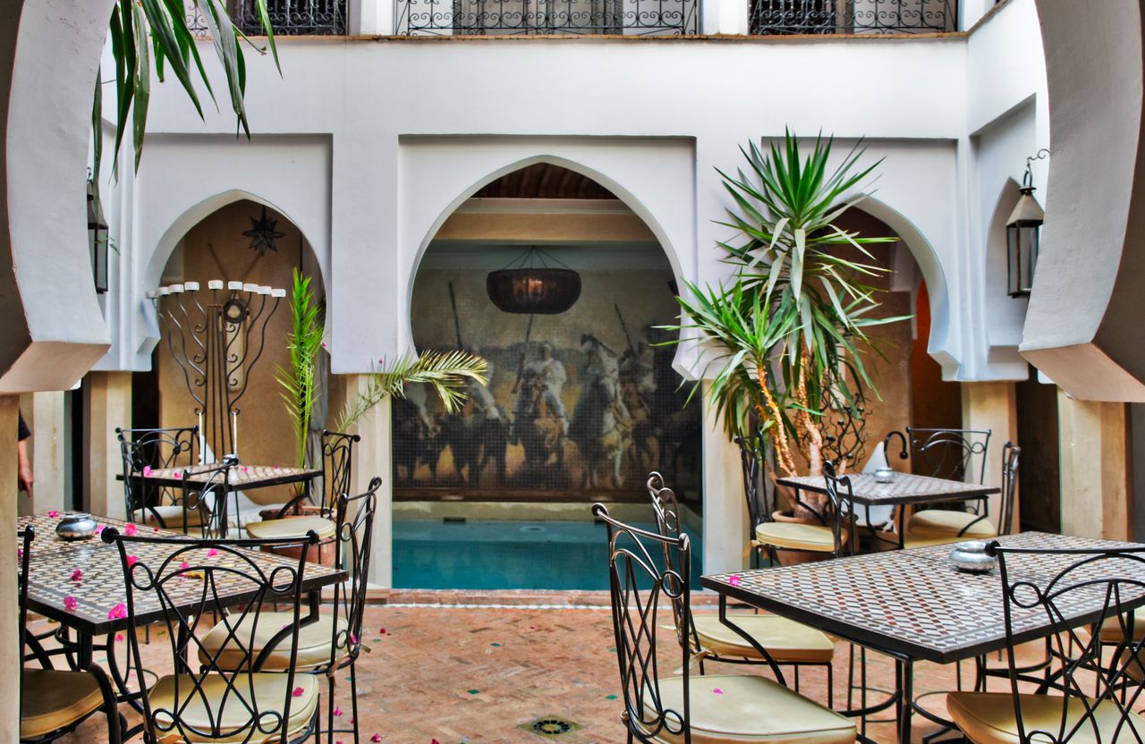 Charming Moroccan courtyard design featuring ornate tables, chairs, and a small pool, creating a relaxing ambiance.